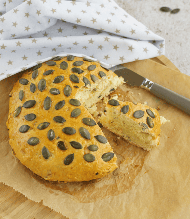 Fresh pumpkin seed cake with a slice cut out, on a wooden board with a knife.
