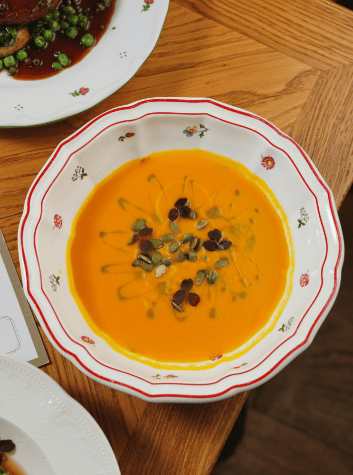 Bowl of creamy pumpkin soup garnished with seeds on a decorative plate.